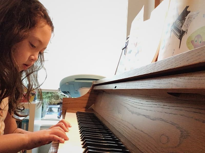 Child looks at her hands while playing piano during an online piano lesson