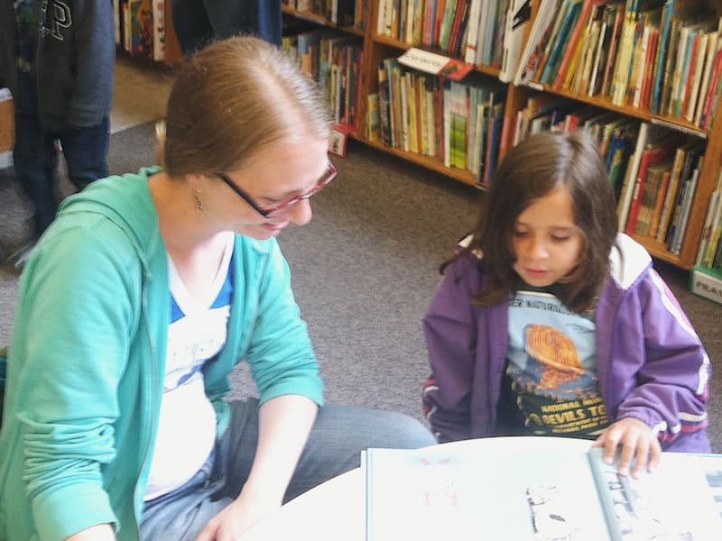 Sarah helping a young student read during a library visit