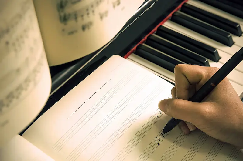 Music student writes music notes on manuscript paper which is resting on their piano