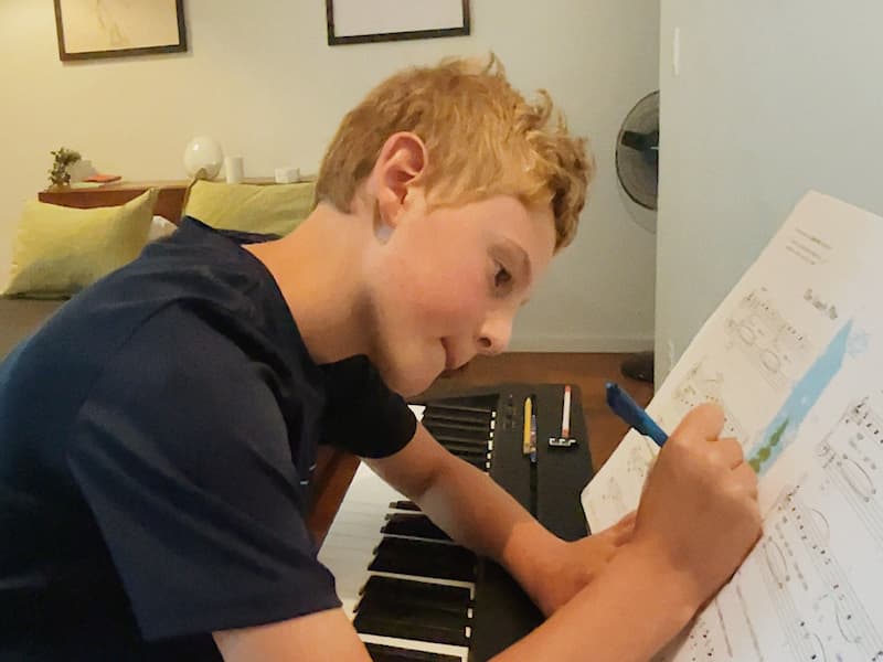A piano student leans over his keyboard to write on his music with a pencil