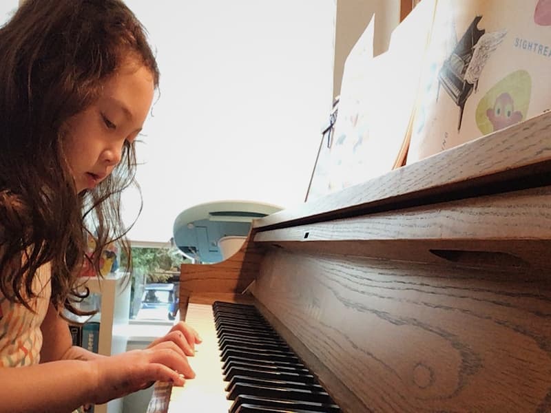 Small child focuses on her hands while playing the piano in an online piano lesson
