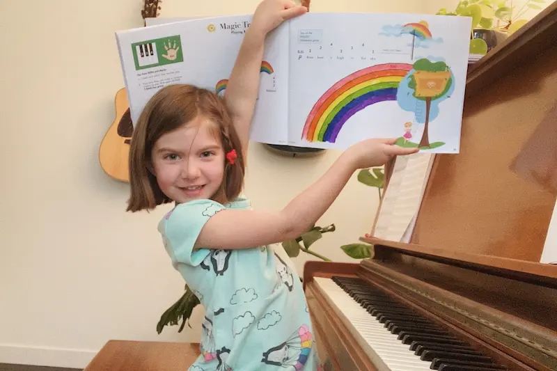 A student joyfully holds up her sheet music during an online piano lesson