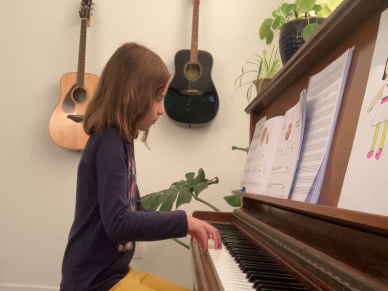 A young girl plays piano with round hands and guitars behind her