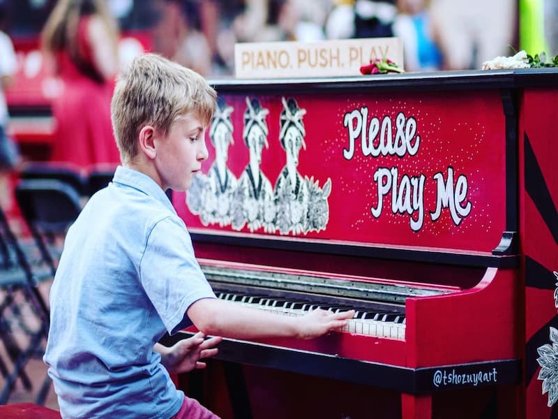 Blonde boy in light blue collared shirt playing a red piano